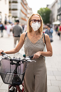 妇女用自行车在行人城市街道上走路 在公共场合戴医疗面罩 以防止科罗纳病毒传播 在贪食流行期间是新常态社会男人街道疾病流感责任感太图片