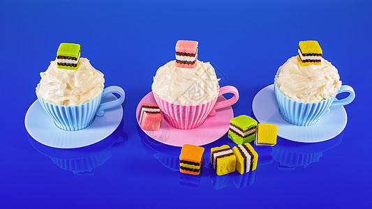 以蓝背景糖果为装饰的杯饼彩虹蓝色鞭打生日烹饪派对茶杯杯子甜点漩涡图片