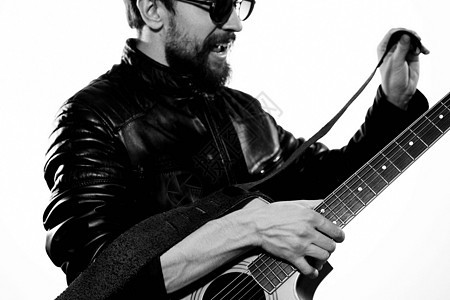 一个男人在黑色皮夹克里弹吉他 戴墨镜 背景浅薄音乐家音乐低音乐趣工作室展示居住成人艺术家歌曲图片