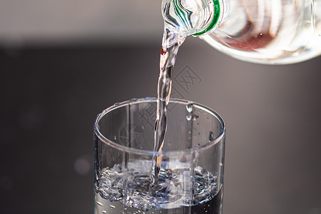 将塑料瓶的水从塑料瓶倒入一个模糊的背面玻璃杯图片