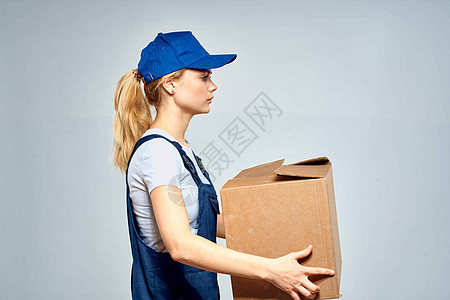 一名身穿工作制服 手里拿着一个盒子的女性 在送货服务的灯光背景下纸盒成人工作室微笑运输职业蓝色商业导游女士图片