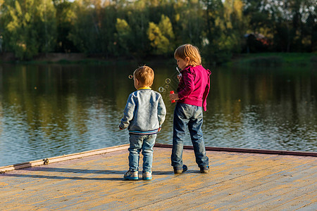 一个小男孩和一个女孩站在一座城市公园的池塘附近的木地板上图片