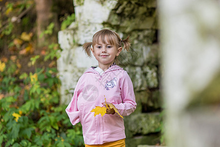 一个手臂折断的女孩站在一个旧公园的砖墙附近女士情感建筑孩子女性青年裙子微笑叶子建筑学图片