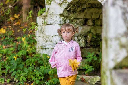 一个手臂折断的女孩站在一个旧公园的砖墙附近建筑裙子孩子女士女性叶子建筑学金发情感微笑图片