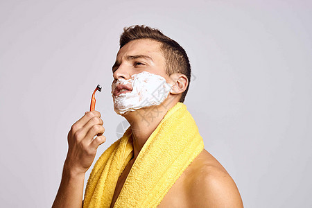 一个肩上披着黄毛巾和橙色剃刀白色白泡沫清洁皮肤的男人治疗身体成人温泉浴室微笑剃须卫生奶油头发图片