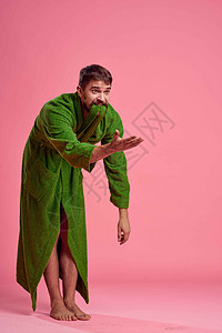 一个身穿绿色长袍 在粉红色背景中完全成长的情绪化男人用手向模特做手势工作室成人姿势幸福快乐咖啡微笑男性卫生浴衣图片