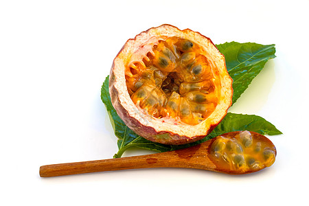 Maracuja在小玻璃容器里用木勺和白底的叶子将水果切成半截整片 果实黄色 果汁和种子宏观热带饮食食物热情情调甜点玻璃茶匙勺子背景图片
