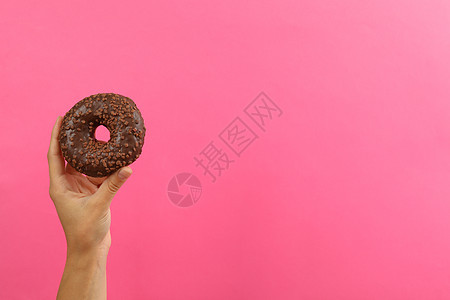 女性手握着粉红背景的美味甜甜圈图片