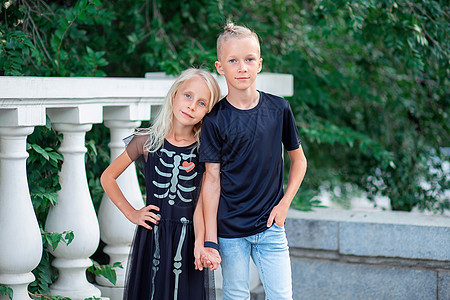 现代孩子 穿黑色长袍的兄妹站在手把手边上 万圣节礼服上的Skeleton图案图片