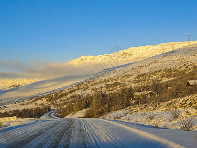 在金色日出时驾驶 穿过挪威的山林和森林爬坡运输街道雪景阳光农村旅行树木金光山脉图片