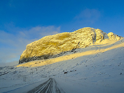 日出时驾车穿过挪威的山脉和森林降雪太阳街道旅行树木农村运输雪景蓝色小路图片