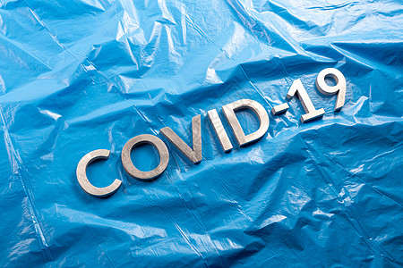 CCOVID-19用铝字母拼贴在压成蓝色塑料胶片背景上 以平面成形 对角视角图片