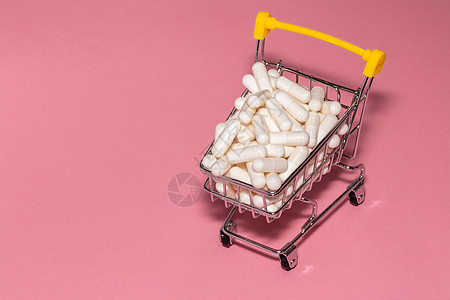 一个装满白色药丸的小购物车的高角度拍摄 粉红色的背景 复制空间 在线购物 购买药品 制药业务概念图片