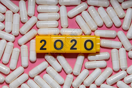 白色药丸的顶部特写镜头围绕着带有黑色数字的黄色立方体 形成 2020 年 粉红色的背景 医疗保健 医疗和制药概念 新常态和现实概图片