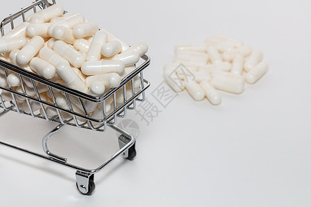 装满白色药丸的小购物车的高角度拍摄 一堆药丸在背景中模糊 白色背景 特写镜头 网上购物 买药 制药企业概念图片