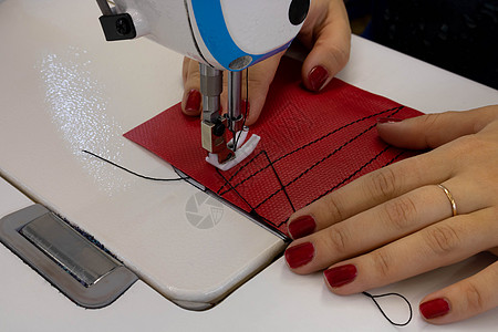 女裁缝在缝纫机上用红布缝制衣服 带活套和压脚特写的钢针工具工艺工厂剪裁材料作坊下水道纺织品行动裙子图片