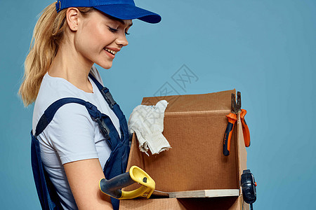身穿制服 手拿盒子的职业女性工具装载送货服务蓝色背景工人商业女士工作室工作导游成人微笑女孩运输图片