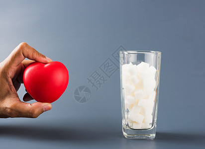 手握心脏靠近装满白糖的玻璃杯疾病糖果国际立方体甜点团体饮食葡萄糖水晶糖尿病图片