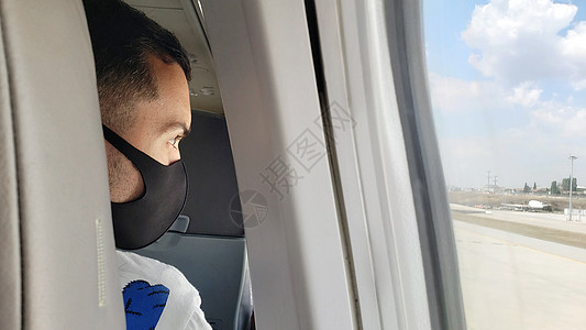 飞机上一名蒙面人看着窗外的窗户 在科罗纳病毒流行期间 空中旅行以及预防乘客空气游客旅游假期运输疾病座位感染图片