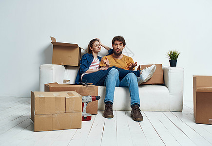 男人和女人坐在沙发上 用一箱工具在室内移动互联网长椅闲暇拥抱家庭妻子娱乐幸福女朋友控制图片
