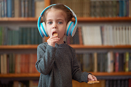 穿着白色大耳机的白人可爱小女孩 在内地用书架的背景来听音乐 笑声快乐乐趣打碟机孩子图书女孩幼儿园女性金发娱乐图片