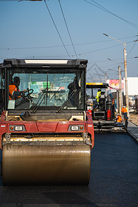 带有重型振动压路机的沥青压路机在道路施工现场的路面上压新的热沥青 在沥青路面工作的重的振动路辗 修复驾驶建筑工程维修压实机车辆城图片