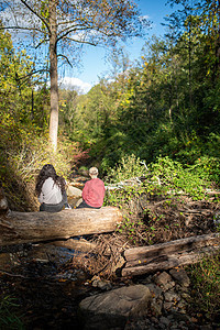两个人在风景森严的森林溪流上的原木上休息图片
