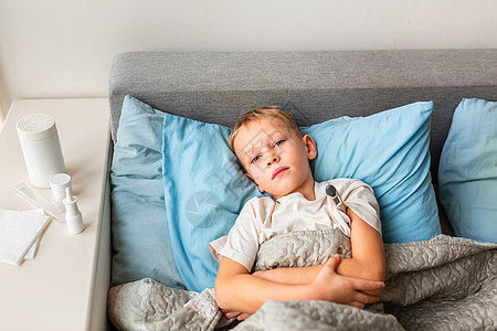 高发和头痛的生病小男孩躺在床上 拿着温度计 在科罗纳病毒流行时留在家中病人儿子沙发枕头温度保健孩子眼睛流感疼痛图片
