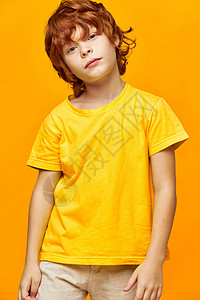 穿着T恤衫和裤子的黄黄色背景红发男孩顶着头部图片