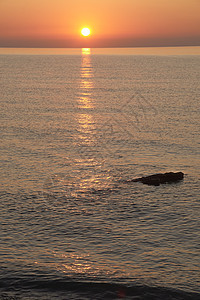 太阳升起在岩石海滩上橙子日落海洋辉光海岸阳光海景假期天空紫色图片