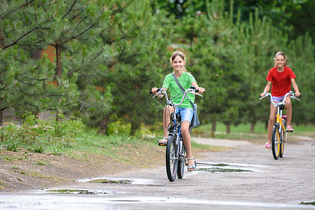 两个女孩在温暖的雨天骑自行车图片
