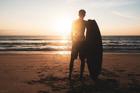 冲浪男子在日落 bea 上背着冲浪板的休眠日出假期晴天旅行木板乐趣热带海景男性冲浪者图片