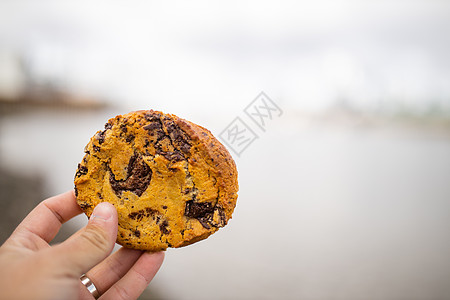 手握着巧克力薯片饼干和布蓝利灰河作为背景城市阳光旅行小吃全景摩天大楼风景脆片码头建筑学图片