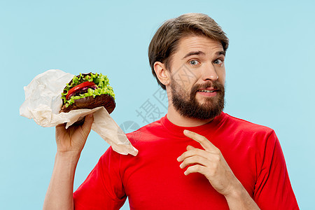 手上拿着汉堡包的男人 快速食物饮食 红T恤蓝背景图片