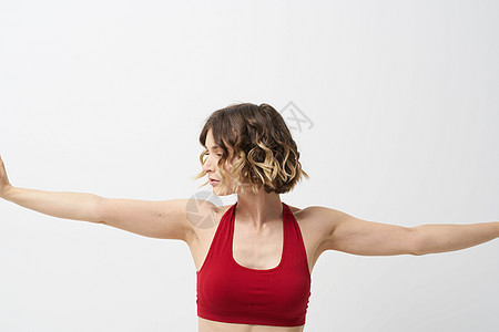 女孩在轻光背景下做瑜伽 用他的双手穿红色T恤领汗衫健身房专注福利身体力量女士成人沉思活动平衡图片