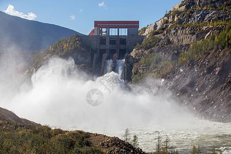 俄罗斯马加丹地区的科雷马水电站 从水力发电站的大坝溢洪道 一条巨大的水流在高山的背景下流入河流发电机水库水电电气阳光技术流动溪流图片