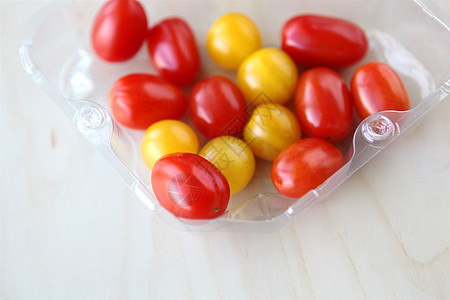 在木制桌上的塑料盒中选择樱桃西红柿黄色和红色图片