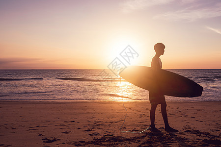冲浪男子在日落 bea 上背着冲浪板的休眠太阳冒险活动闲暇假期海洋日出热带生活方式娱乐图片