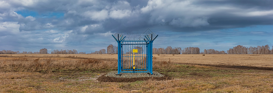 围栏顶部带铁丝网的笼式工业加油站的全景照片 笼子中间的黄色煤气管 栅栏上的空盘子 多云的天空作为背景 俄罗斯西伯利亚图片