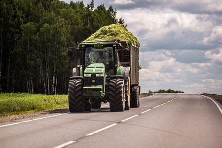 俄罗斯图拉 — 2019 年 7 月 30 日 在夏季道路上滚动的拖车中装有绿色青贮饲料的拖拉机图片