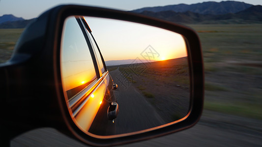 在车的侧面镜子里看到车辆太阳日出交通天空地平线阳光运动丘陵运输图片