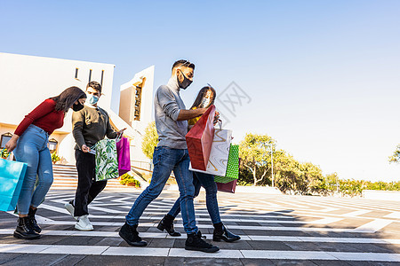 年轻朋友们在城市广场的户外散步 对戴着冠状病毒安全防护面具的购物感到满意 — 穿着休闲服的漂亮人带着购物袋在户外玩得开心图片