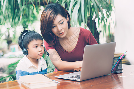 年轻的亚洲母子使用笔记本电脑在家学习和学习 男孩戴着耳机进行远程电子学习 老师或妈妈支持孩子 教育理念家庭技术男生导师冲浪瞳孔社图片