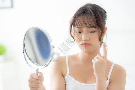 美丽的年轻亚洲女性在卧室里照镜子 脸上有粉刺问题 脸上有美容问题 青春痘治疗 亚洲女孩长痘痘 有忧虑和不快 护肤和健康理念皮肤疙图片