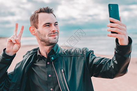 英俊的青年在海滩自以为是的家伙博客视频男人冒充博主男性皮夹克潮人电话手机图片