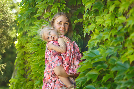 一个穿着浅色夏日太阳裙的迷人女孩和她的小女儿在一个绿色的公园里散步 把她抱在怀里 享受温暖阳光明媚的夏日婴儿拥抱帽子喜悦微笑母亲图片