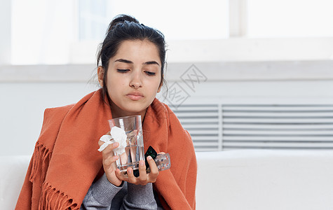 手握有玻璃和餐巾的橙色格子过敏反应模型的妇女女性感染药品鼻子发烧痛苦温度长椅沙发枕头图片