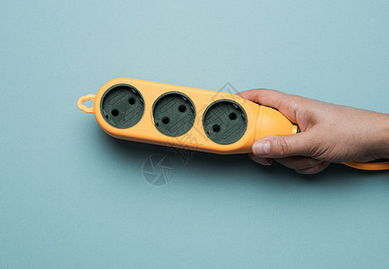 手握橡胶橙色电源条 蓝色背景有三个插座图片