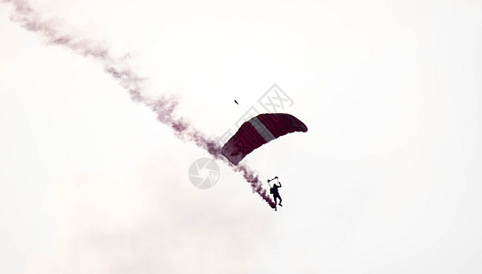 在空中展览期间 剪影降落伞特技在空中滑行时没有聚焦和模糊 带着红色的烟雾痕迹翅膀运动空气红烟危险男人烟迹自由橙子活动背景