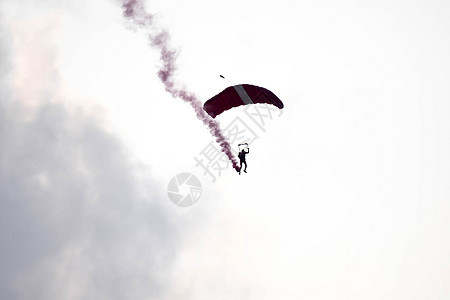 在空中展览期间 剪影降落伞特技在空中滑行时没有聚焦和模糊 带着红色的烟雾痕迹飞机冒险活动跳伞员橙子翅膀天空自由跳伞风险图片